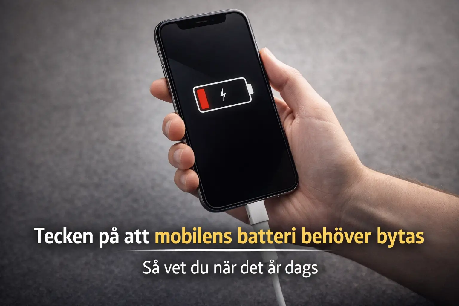 En hand håller en smartphone som visar en ikon för låg batterinivå medan den laddas. Den svenska texten på bilden lyder: "Tecken på att mobilens batteri behöver bytas. Så vet du när det är dags.